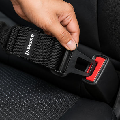 A close-up of a hand fastening a black car seat belt with a red release button, attached to a black car seat. The brand name 'pawsa' is visible on a black label sewn onto the belt strap.